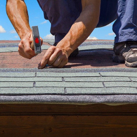 A crouching roofer hammering shingles.