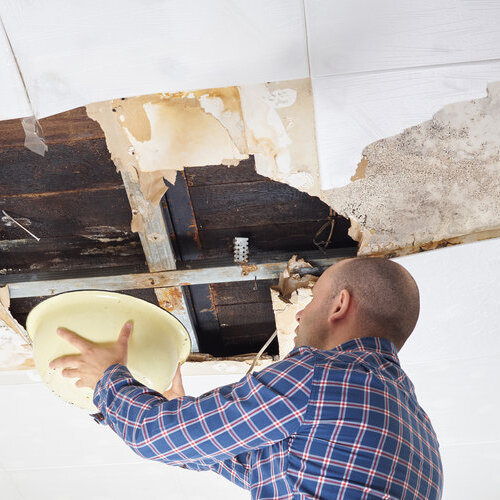 man holding a basin under a leaking hole in the ceiling